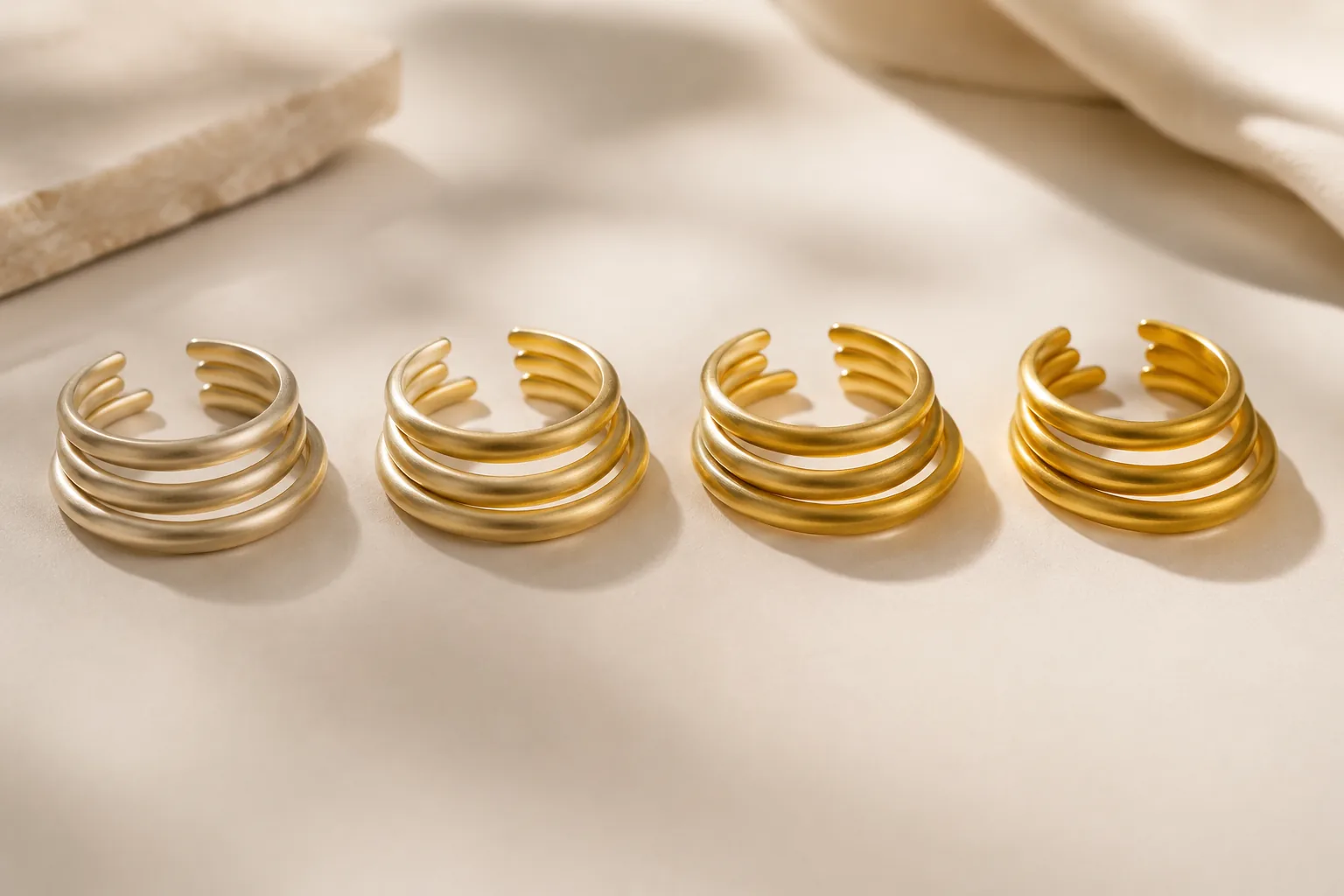 Four groups of plain unbranded gold bands shown in subtly different gold tones for karat comparison.