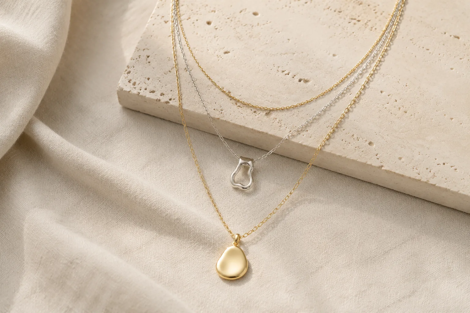 Three layered necklaces arranged at different lengths to show how an initial-inspired pendant can sit without crowding the stack.