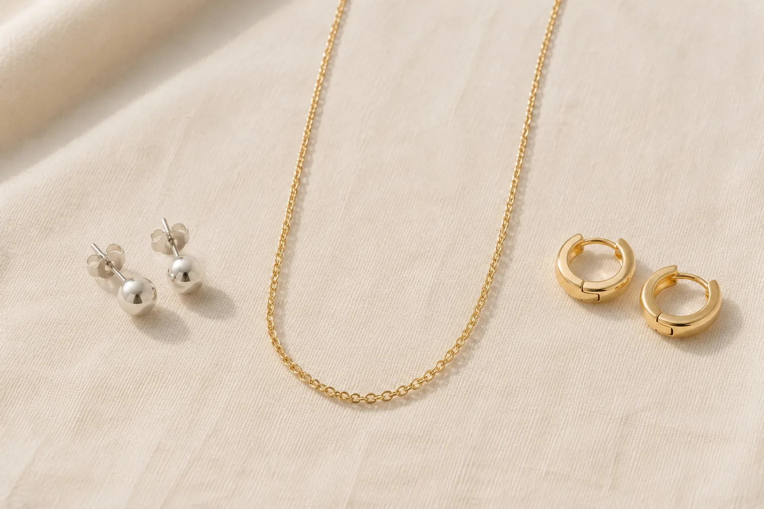 Simple studs, a chain necklace, and small hoops arranged as lower-risk first jewelry pieces.